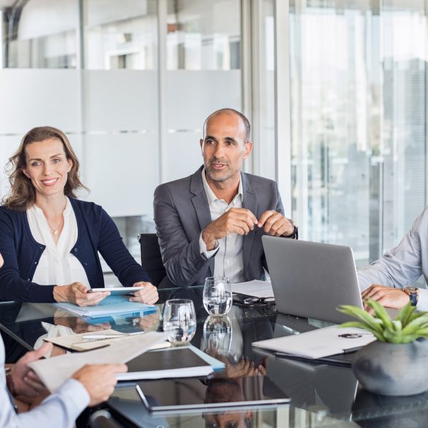 Business meeting Multiethnic group of business people sitting in annual meeting in conference room. Mature leader with businessmen and businesswomen discussing. Busy partners working together in modern office.